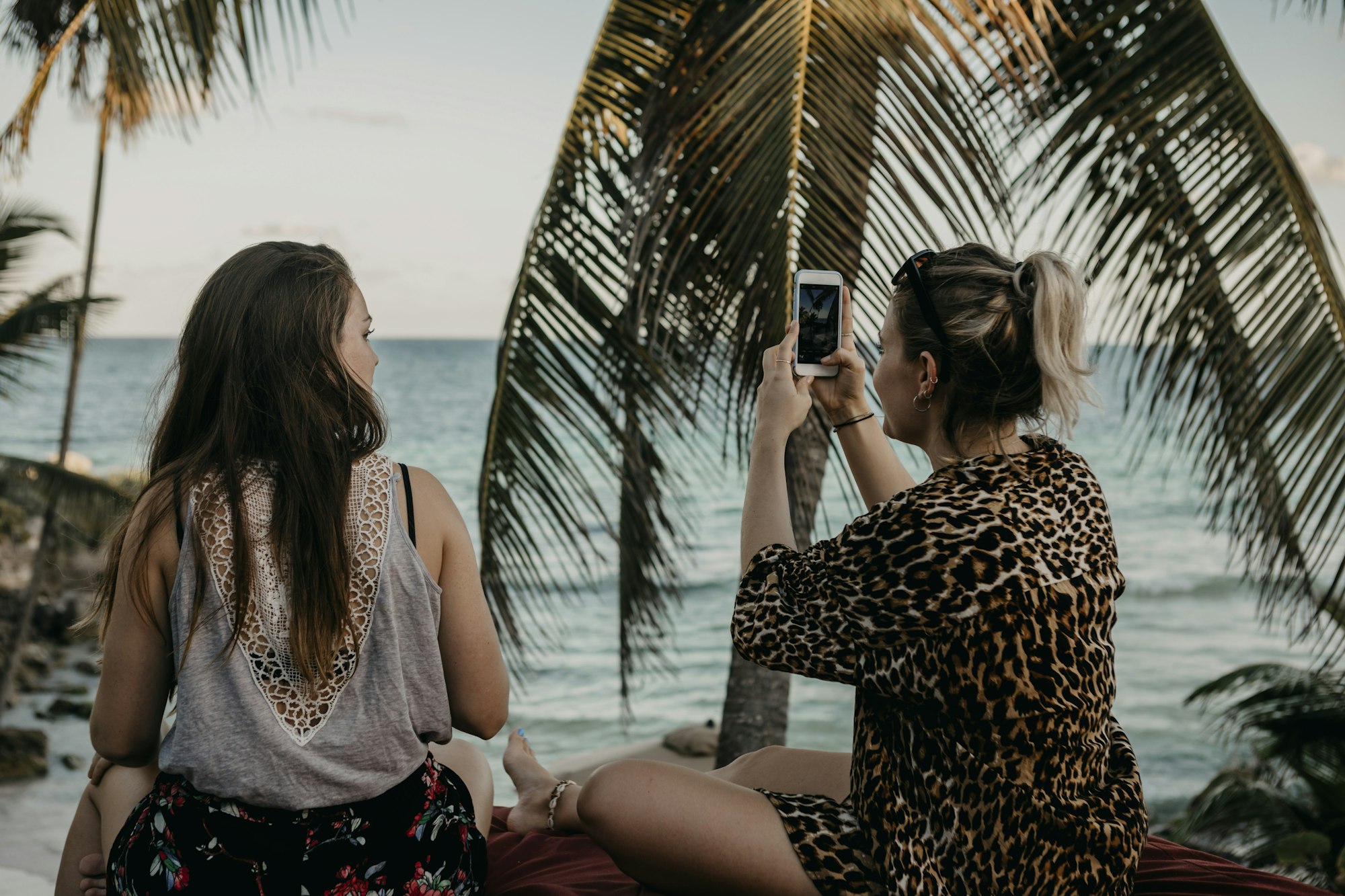 Mexico, Quintana Roo, Tulum, two young women with cell phone relaxing on the beach